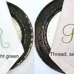 May include: Two cloth napkins, one white and one beige, each folded and placed on decorative plates. The white napkin has a light green embroidered "R", and the beige napkin has a seaweed green "R". The text "Thread, light green" and "Thread, seaweed" are below the napkins.