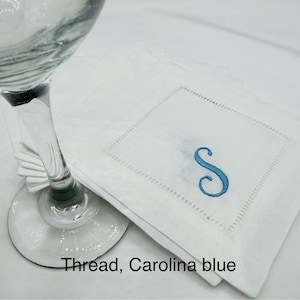 K&ouml;nnte beinhalten: Wei&szlig;e Cocktailservietten aus Leinen mit einem in Carolina-Blau gestickten Buchstaben "S". Die Servietten haben eine quadratische Form mit einer dekorativen, gen&auml;hten Bord&uuml;re. Der Text "Thread, Carolina blue" ist unten im Bild zu sehen.