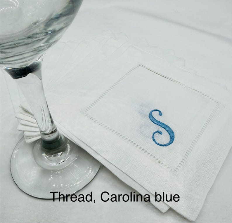 K&ouml;nnte beinhalten: Wei&szlig;e Cocktailservietten aus Leinen mit einem in Carolina-Blau gestickten Buchstaben "S". Die Servietten haben eine quadratische Form mit einer dekorativen, gen&auml;hten Bord&uuml;re. Der Text "Thread, Carolina blue" ist unten im Bild zu sehen.