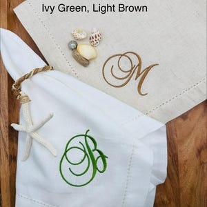 May include: White linen napkin with a green embroidered "B" and a beige napkin with a brown embroidered "M". A starfish and seashells are included. The text "Thread Ivy Green, Light Brown" is visible.