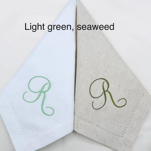 May include: Two folded linen napkins, one white and one beige, each embroidered with the letter "R" in light green and seaweed green, respectively. The text "Light green, seaweed" is above the napkins.