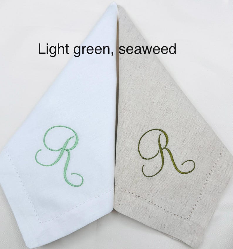 May include: Two folded linen napkins, one white and one beige, each embroidered with the letter "R" in light green and seaweed green, respectively. The text "Light green, seaweed" is above the napkins.