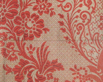 May include: A detailed close-up of a fabric with a repeating floral pattern. The design features large, stylized red flowers and foliage against a light beige background with a grid-like texture. The pattern is symmetrical and ornate.