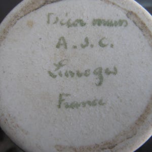 Puede incluir: Primer plano de la base de un jarr&oacute;n de cer&aacute;mica blanca. La base presenta texto manuscrito verde descolorido: "Dian mum, A.S.C., Limoges, France."