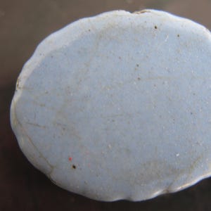 Puede incluir: Una piedra azul claro de forma irregular con una superficie texturizada. La piedra tiene un borde ligeramente irregular y parece estar hecha de un material s&oacute;lido. Se ven peque&ntilde;as motas oscuras en la superficie.