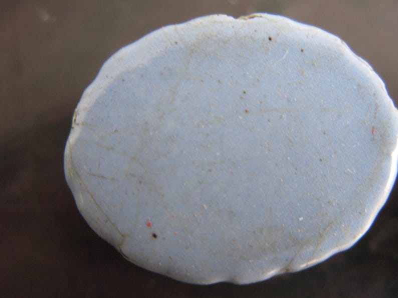 Puede incluir: Una piedra azul claro de forma irregular con una superficie texturizada. La piedra tiene un borde ligeramente irregular y parece estar hecha de un material s&oacute;lido. Se ven peque&ntilde;as motas oscuras en la superficie.