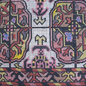 K&ouml;nnte beinhalten: Eine Nahaufnahme eines bunten Teppichs mit geometrischem Muster. Der Teppich besteht aus kleinen Quadraten in verschiedenen Farben, darunter Rot, Gelb, Blau, Pink und Schwarz. Das Muster ist symmetrisch und zeigt ein sich wiederholendes Design aus Blumen und Bl&auml;ttern.