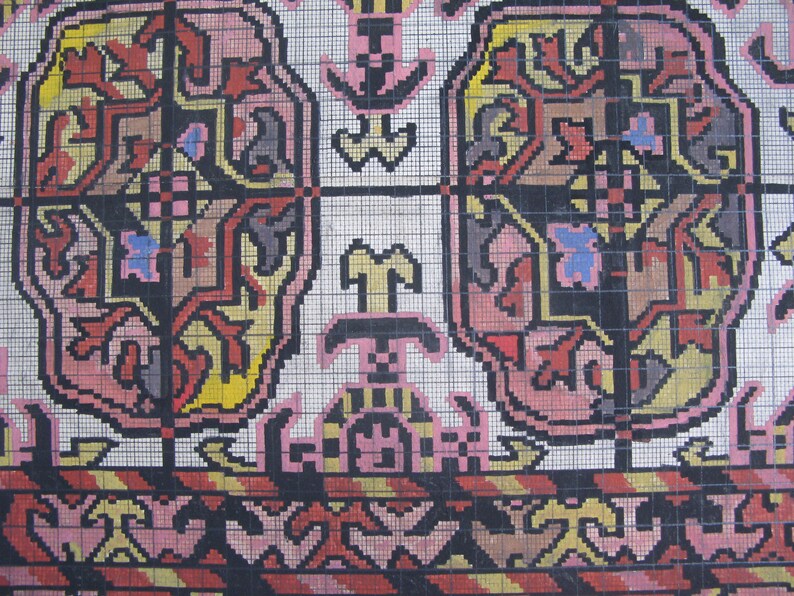K&ouml;nnte beinhalten: Eine Nahaufnahme eines bunten Teppichs mit geometrischem Muster. Der Teppich besteht aus kleinen Quadraten in verschiedenen Farben, darunter Rot, Gelb, Blau, Pink und Schwarz. Das Muster ist symmetrisch und zeigt ein sich wiederholendes Design aus Blumen und Bl&auml;ttern.
