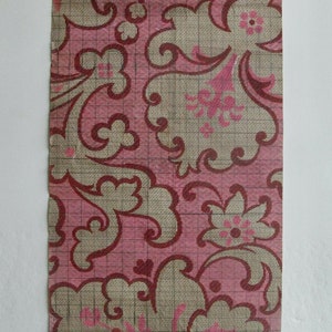 Puede incluir: Una muestra de papel tapiz vintage con un patrón floral rosa y beige. El patrón presenta un diseño repetitivo de flores y hojas estilizadas. El papel tapiz tiene un patrón de cuadrícula impreso en él.