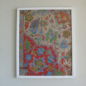 Puede incluir: Obra de arte enmarcada con un detallado patrón floral en tonos rojos, azules, verdes y dorados. El diseño se encuentra sobre un fondo beige con una superposición de cuadrícula, encerrado en un marco blanco. La obra evoca una estética vintage.