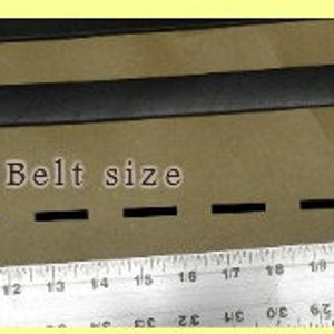 May include: A black leather belt with a metal buckle, measured on a ruler to be 25 inches long. The text "Belt size" is written on the surface below the belt.