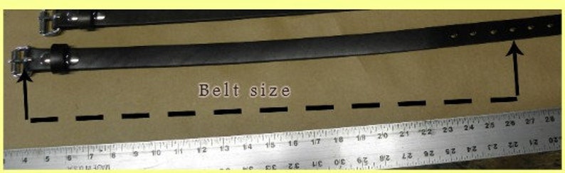May include: A black leather belt with a metal buckle, measured on a ruler to be 25 inches long. The text "Belt size" is written on the surface below the belt.