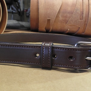 May include: A brown leather belt with a silver buckle. The belt is stitched with a brown thread and has two rows of stitching.