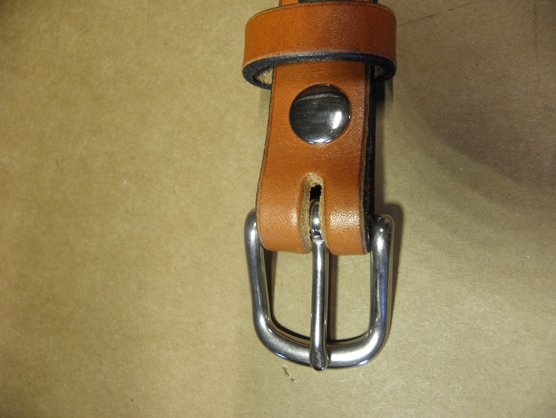 May include: Close-up of a brown leather belt with a silver buckle. The buckle has a smooth, rounded finish and a simple design.