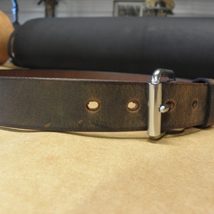 May include: A dark brown leather belt with a silver buckle and multiple holes. The belt is worn and has a distressed look.