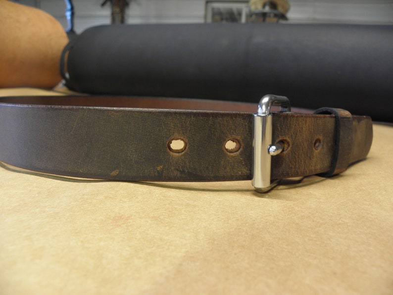 May include: A dark brown leather belt with a silver buckle and multiple holes. The belt is worn and has a distressed look.