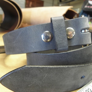 May include: A dark gray leather belt with a silver buckle and two silver rivets. The belt is folded in half and the buckle is visible.