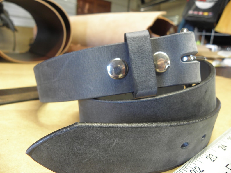 May include: A dark gray leather belt with a silver buckle and two silver rivets. The belt is folded in half and the buckle is visible.