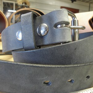 May include: A dark gray leather belt with a silver buckle and two silver rivets. The belt is folded in half and the buckle is visible.