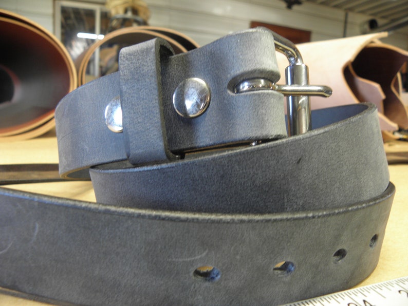 May include: A dark gray leather belt with a silver buckle and two silver rivets. The belt is folded in half and the buckle is visible.