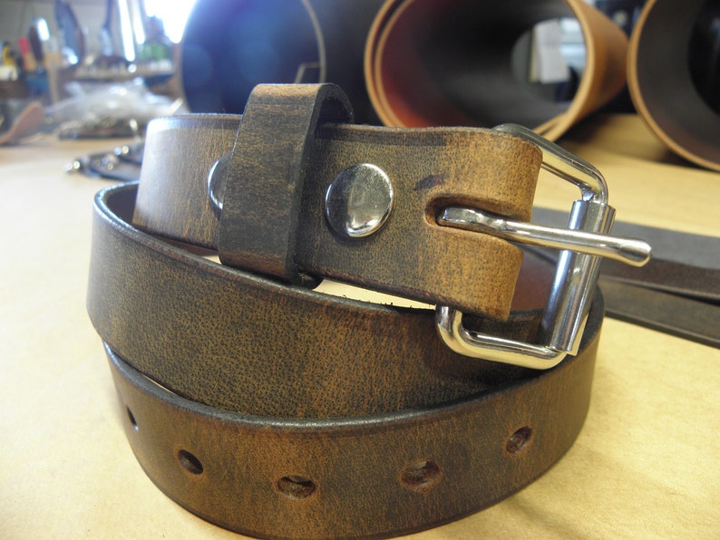 May include: A brown leather belt with a silver buckle. The belt is folded in half and the buckle is visible. The belt is made of a distressed leather.