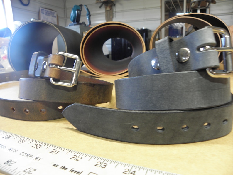May include: A close-up of four leather belts, two brown and two black, with silver buckles. The belts are arranged in a stack, with the brown belts on top and the black belts on the bottom.