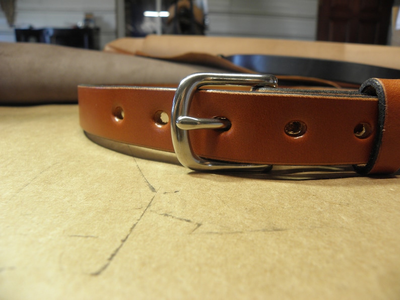May include: A brown leather belt with a silver buckle. The belt has multiple holes for adjusting the fit.