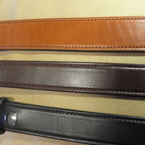May include: Three leather belts in different colors: brown, dark brown, and black. Each belt has a stitched edge and a metal buckle.