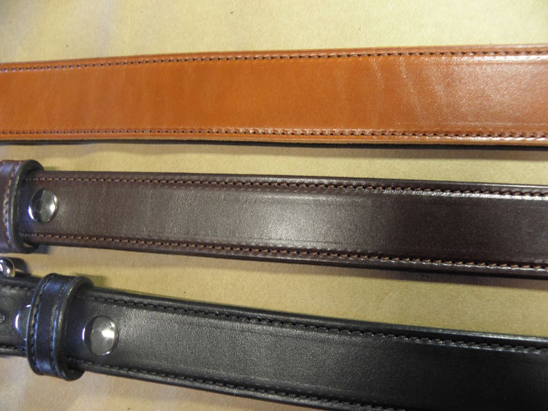 May include: Three leather belts in different colors: brown, dark brown, and black. Each belt has a stitched edge and a metal buckle.
