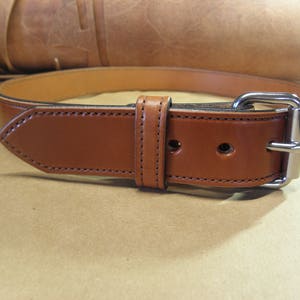 May include: A brown leather belt with a silver buckle. The belt is stitched with a contrasting thread.