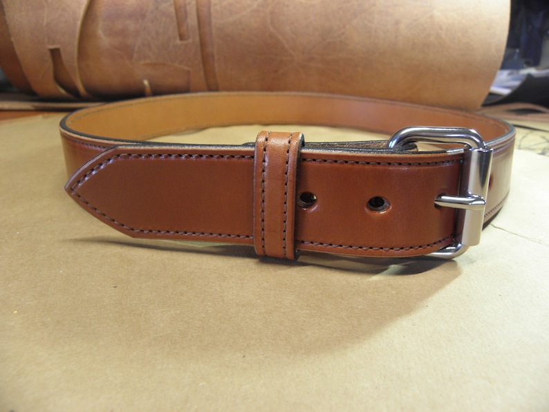 May include: A brown leather belt with a silver buckle. The belt is stitched with a contrasting thread.