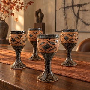 May include: Four ceramic goblets featuring a dark, speckled black and brown glaze. Each vessel has a wide, textured band around the upper portion decorated with a repeating geometric diamond and petal pattern in a contrasting light brown clay.