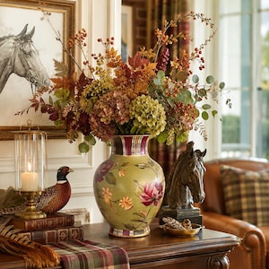 May include: A ceramic vase with a light green base, decorated with painted floral motifs and a plaid rim, filled with an arrangement of autumn-colored foliage, dried hydrangeas, and red berries, displayed on a wooden surface with decor.