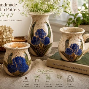 May include: A set of three handmade studio pottery pieces including a vase, a mug, and a multi-use vessel. Each piece is cream-colored with brown speckles and features a hand-painted blue iris flower design with green leaves and stems.