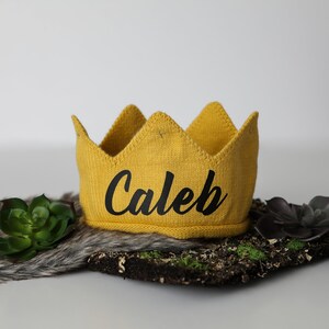 May include: A yellow knitted crown with the name "Caleb" embroidered in black.