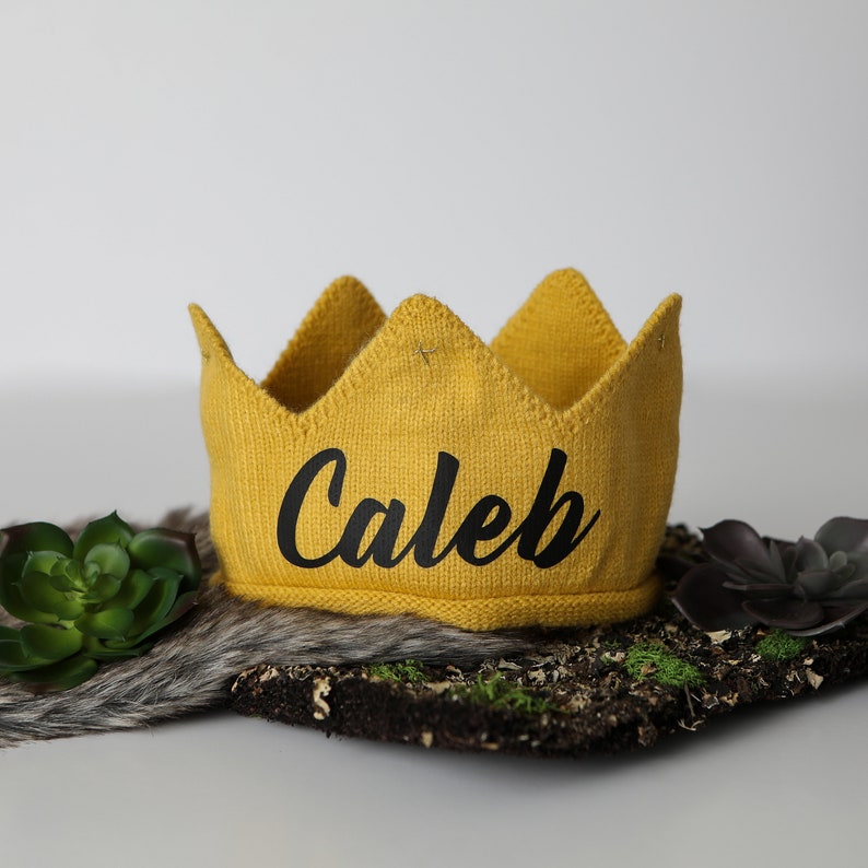 May include: A yellow knitted crown with the name "Caleb" embroidered in black.