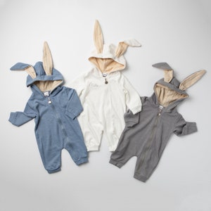 May include: Three baby bunny onesies in blue, white, and gray. The white onesie has the word "Max" embroidered on the front.