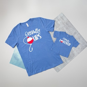 May include: Two blue t-shirts with a fishing theme. The larger shirt says "Fish-ally Ours" with a red and white fishing bobber and hook. The smaller shirt says "Fish-ally Forever".