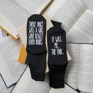 May include: A pair of black socks with white text. One sock reads "There once was a girl who really loved books." The other sock reads "It was me. The end."