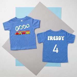 May include: Two blue t-shirts with a train design and the word "FOUR" on one shirt and the name "FREDDY" and the number "4" on the other shirt.