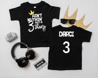Puede incluir: Dos camisetas negras con texto blanco. Una camiseta dice "Ain't nothin' but a 3 thang" con una corona dorada sobre el texto. La otra camiseta dice "Darci 3".