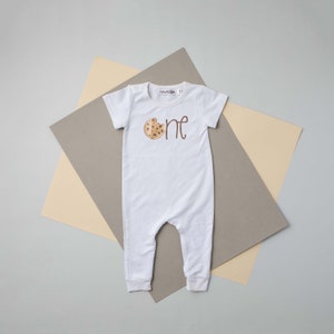 May include: White baby onesie with a brown cookie graphic and the word "one" in brown script.