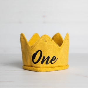 May include: Yellow knitted crown with the word "One" in black lettering.