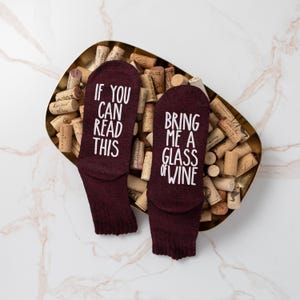 May include: A pair of burgundy socks with white text. One sock says "If you can read this" and the other sock says "Bring me a glass of wine".