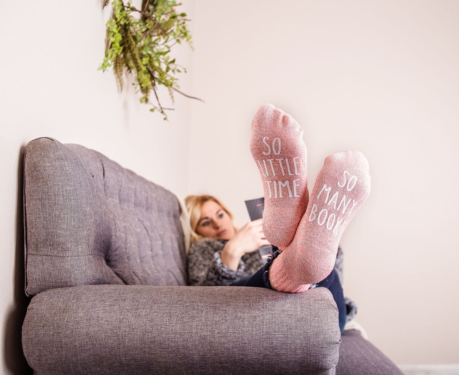 a woman lying on a couch with pink socks that say "so little time" on one foot, and " "so many books" on the other