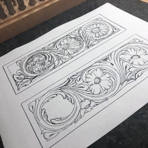 May include: Two black and white line drawings of floral patterns on a white sheet of paper. The patterns are framed by rectangular borders.