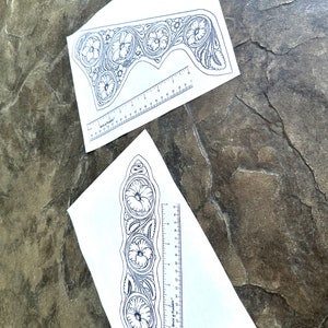 May include: Two black and white leather carving patterns on white paper with rulers. The top pattern is a floral design with a curved top. The bottom pattern is a floral design with three flowers.