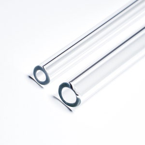 May include: Two clear glass drinking straws, one on top of the other, with a slight angle. The straws are smooth and have a rounded edge.