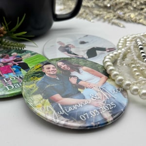 Puede incluir: Tres posavasos redondos con fotos y texto personalizados. Un posavasos presenta una foto familiar con el texto "We Love Dad". Otro posavasos muestra una pareja con el texto "Julianna & Nico 07.03.2025". Una taza negra y elementos decorativos están en el fondo.