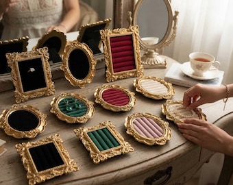 May include: A collection of ornate, gold-colored jewelry display trays and frames. The trays feature velvet inserts in various colors, including red, green, and pink. Some frames hold rings and earrings, while others are empty.